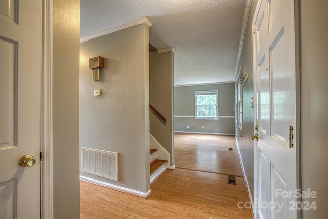 hall featuring a textured ceiling, light hardwood / wood-style flooring, and ornamental molding