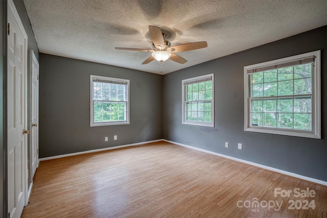 unfurnished room with a textured ceiling, light wood-type flooring, and ceiling fan