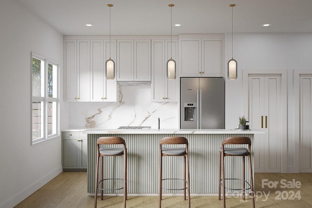 kitchen with light wood finished floors, decorative backsplash, a kitchen breakfast bar, light countertops, and stainless steel refrigerator with ice dispenser