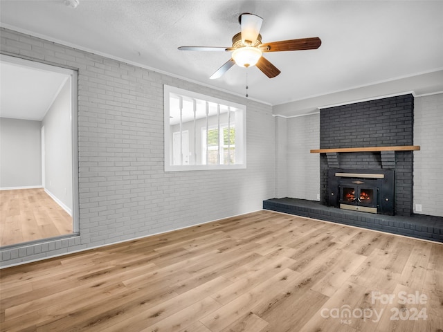 unfurnished living room with ceiling fan, light wood-type flooring, brick wall, a fireplace, and a textured ceiling