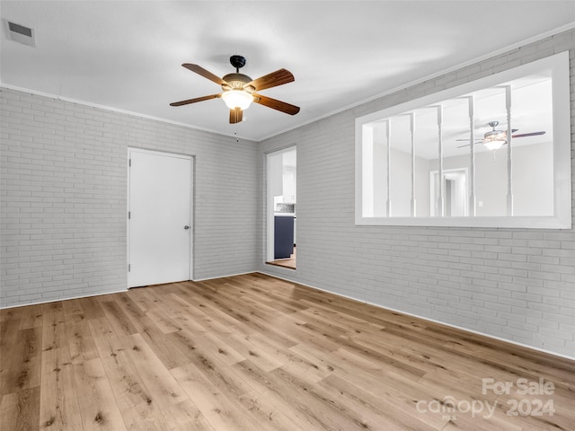 unfurnished room featuring light wood-type flooring, ceiling fan, brick wall, and ornamental molding