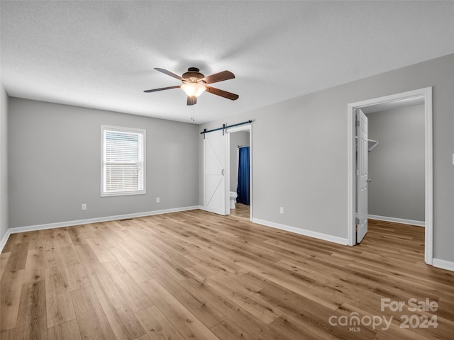 unfurnished bedroom with a barn door, ceiling fan, light wood-type flooring, a closet, and a walk in closet