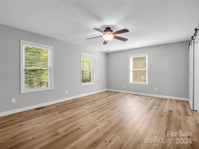 unfurnished room featuring ceiling fan, a barn door, and plenty of natural light