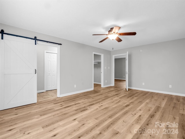 unfurnished bedroom featuring ceiling fan, light hardwood / wood-style floors, a closet, and a barn door