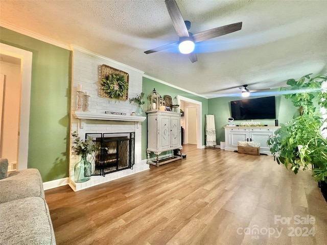 living room featuring ceiling fan, a brick fireplace, crown molding, light wood-type flooring, and a textured ceiling