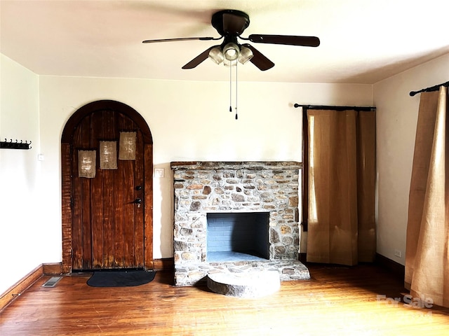 unfurnished living room featuring hardwood / wood-style floors, a stone fireplace, and ceiling fan