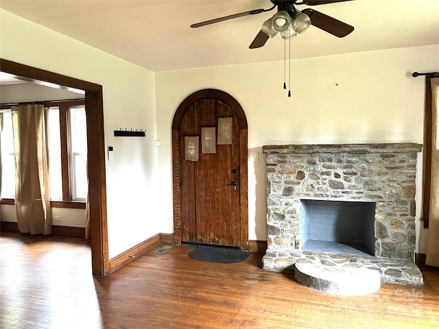 unfurnished living room featuring ceiling fan, a stone fireplace, and dark hardwood / wood-style flooring