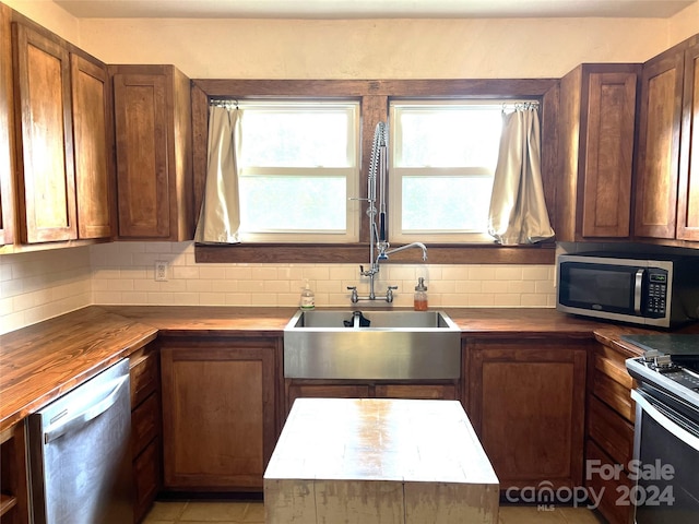 kitchen with appliances with stainless steel finishes, butcher block counters, sink, and backsplash