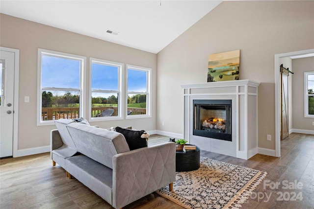 living room with a barn door, high vaulted ceiling, and light wood-type flooring