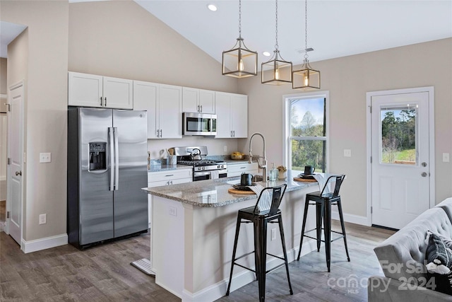 kitchen with an island with sink, white cabinetry, stainless steel appliances, decorative light fixtures, and a breakfast bar