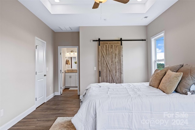 bedroom with connected bathroom, ceiling fan, dark wood-type flooring, and a barn door