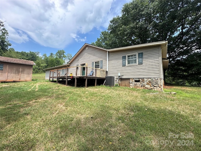 rear view of property with a lawn, central AC, a storage unit, and a deck