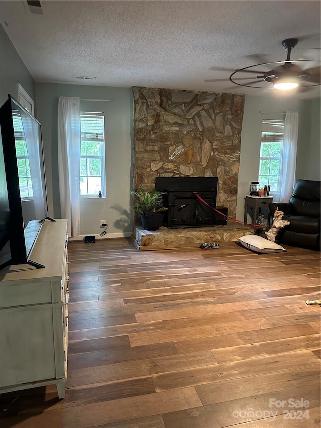 living room featuring a textured ceiling, ceiling fan, hardwood / wood-style floors, and a stone fireplace