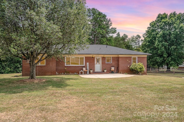 back house at dusk featuring a yard and a patio