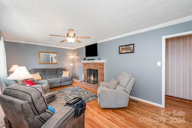 living room with a brick fireplace, hardwood / wood-style floors, crown molding, and ceiling fan