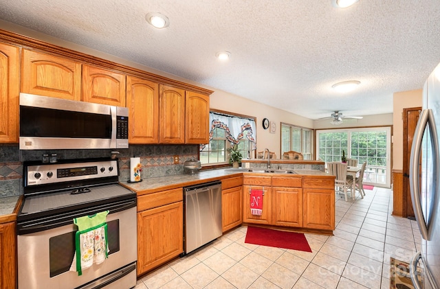 kitchen featuring tasteful backsplash, kitchen peninsula, sink, appliances with stainless steel finishes, and light tile patterned floors