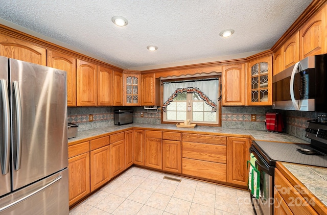 kitchen with tile counters, a textured ceiling, light tile patterned floors, and stainless steel appliances