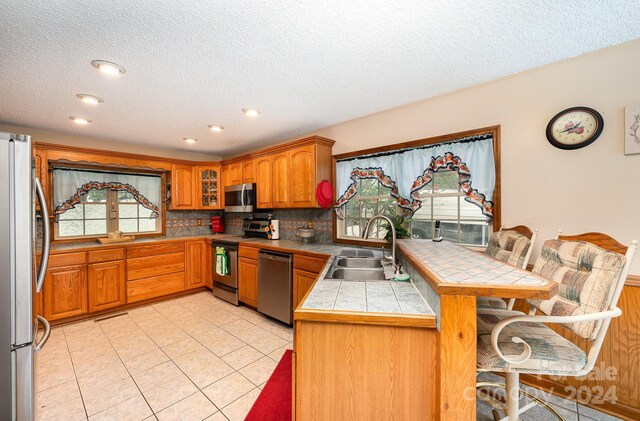 kitchen featuring tile countertops, kitchen peninsula, appliances with stainless steel finishes, a kitchen breakfast bar, and sink