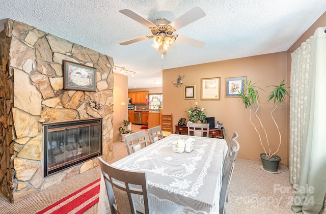 carpeted dining room with track lighting, ceiling fan, a fireplace, and a textured ceiling