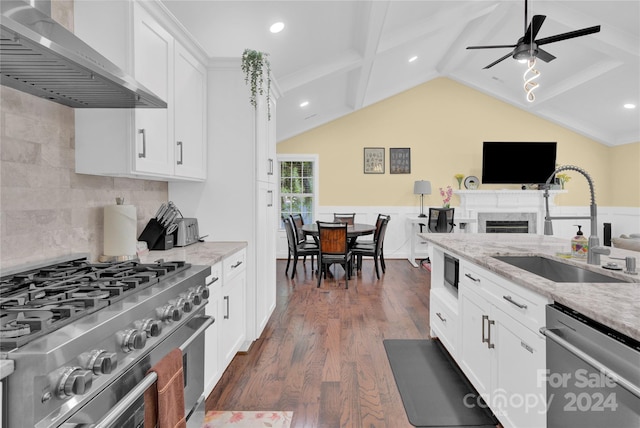 kitchen with stainless steel appliances, wall chimney exhaust hood, white cabinets, light stone counters, and sink