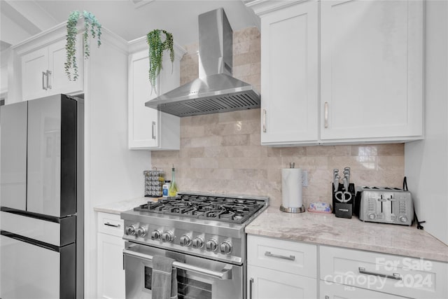 kitchen featuring high end range, white cabinets, wall chimney range hood, backsplash, and fridge