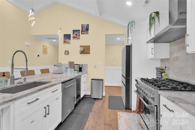 kitchen featuring wall chimney range hood, sink, white cabinetry, hanging light fixtures, and appliances with stainless steel finishes