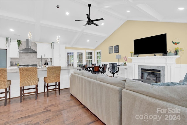 living room with a high end fireplace, french doors, vaulted ceiling with beams, light wood-type flooring, and ceiling fan