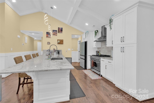 kitchen with white cabinetry, a kitchen bar, stainless steel appliances, wall chimney range hood, and sink