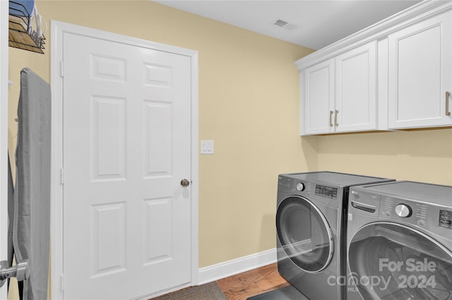 laundry area featuring washing machine and dryer, cabinets, and wood-type flooring