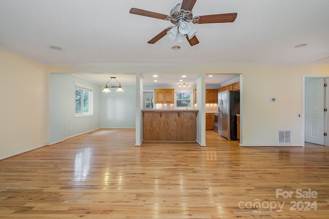 unfurnished living room featuring crown molding, light wood-type flooring, and ceiling fan with notable chandelier