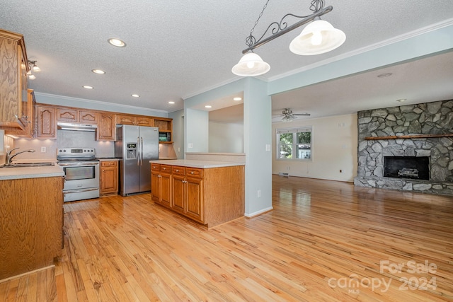 kitchen with light hardwood / wood-style floors, hanging light fixtures, appliances with stainless steel finishes, a stone fireplace, and sink