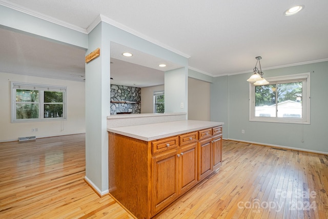 kitchen featuring crown molding, a fireplace, light wood-type flooring, and hanging light fixtures