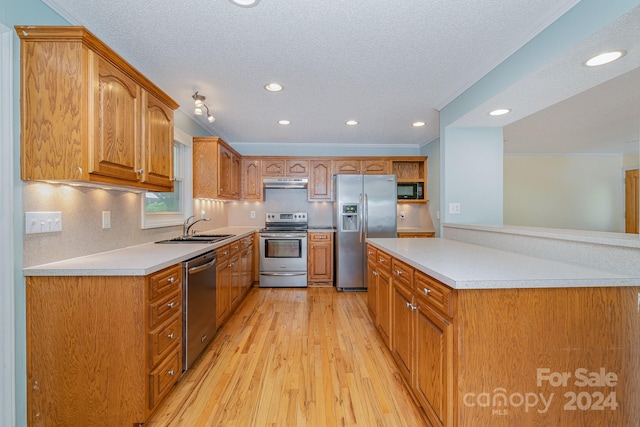 kitchen with sink, appliances with stainless steel finishes, a textured ceiling, and light wood-type flooring