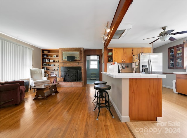 kitchen with built in features, a kitchen breakfast bar, stainless steel refrigerator with ice dispenser, tile counters, and kitchen peninsula