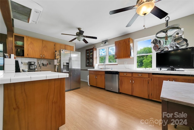 kitchen featuring tile countertops, ceiling fan, stainless steel appliances, light hardwood / wood-style floors, and backsplash