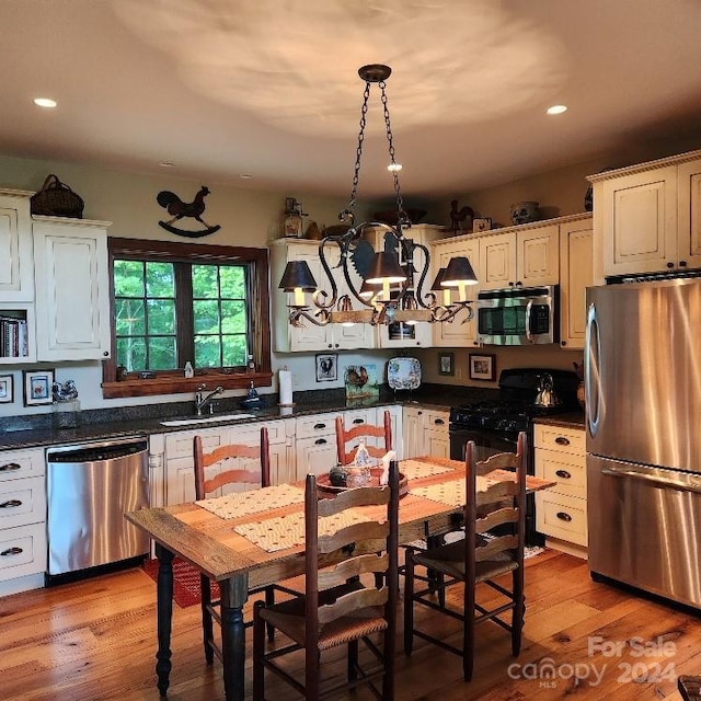 kitchen featuring white cabinetry, light hardwood / wood-style floors, appliances with stainless steel finishes, hanging light fixtures, and sink