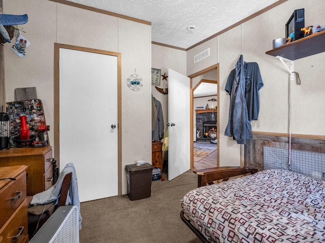 bedroom with carpet floors, a textured ceiling, crown molding, and a stone fireplace