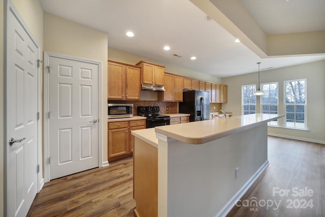 kitchen featuring tasteful backsplash, a center island with sink, black appliances, hanging light fixtures, and light wood-type flooring