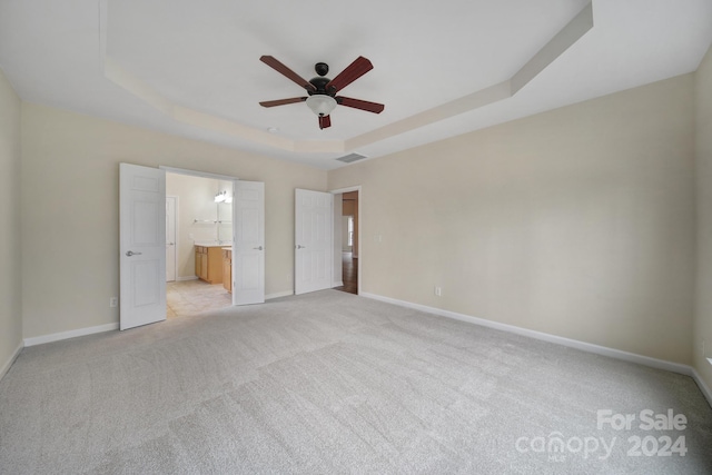 unfurnished bedroom featuring ceiling fan, light colored carpet, a tray ceiling, and connected bathroom