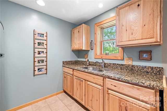 kitchen with light brown cabinetry, sink, and dark stone countertops