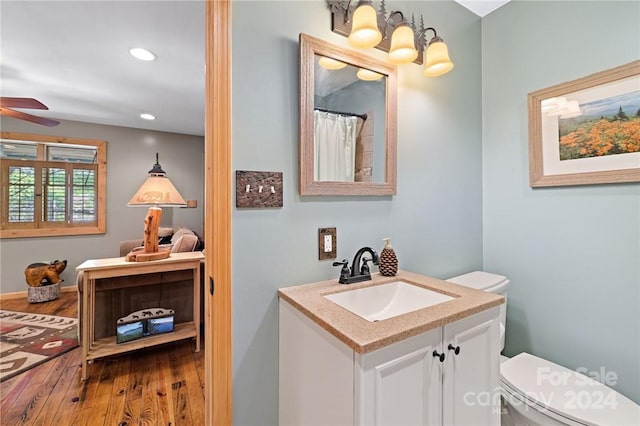 bathroom featuring toilet, vanity, ceiling fan with notable chandelier, and hardwood / wood-style flooring