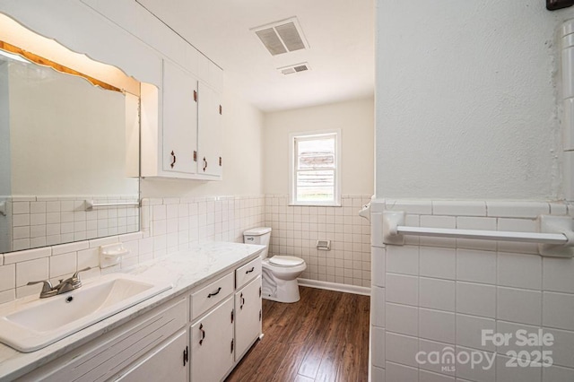 bathroom with wood-type flooring, vanity, toilet, and tile walls