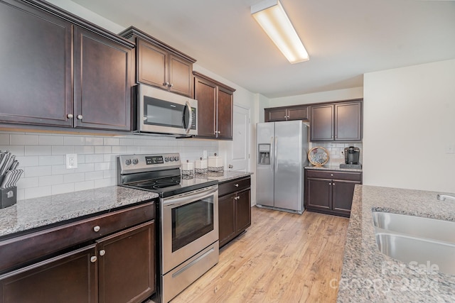 kitchen featuring dark brown cabinetry, stainless steel appliances, light stone countertops, and sink