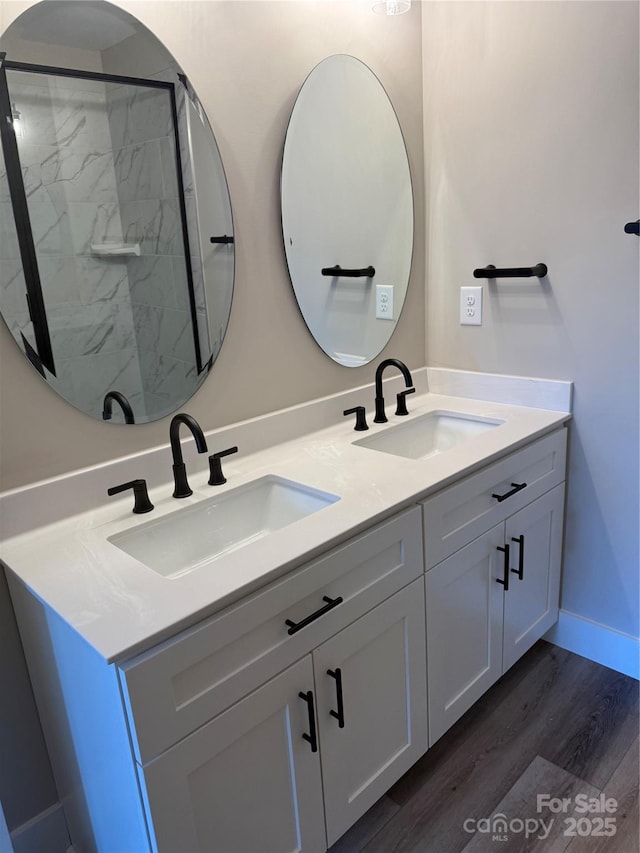 bathroom featuring double vanity, wood finished floors, a shower, and a sink