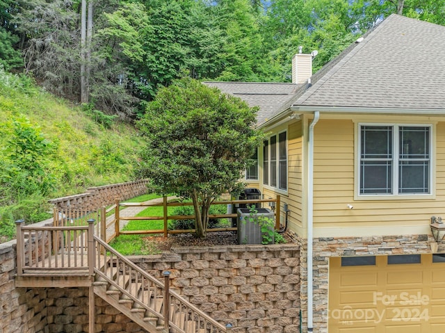 view of side of home with roof with shingles, a chimney, central AC, stone siding, and stairs