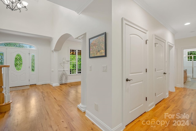 foyer with a notable chandelier, ornamental molding, decorative columns, and light hardwood / wood-style floors