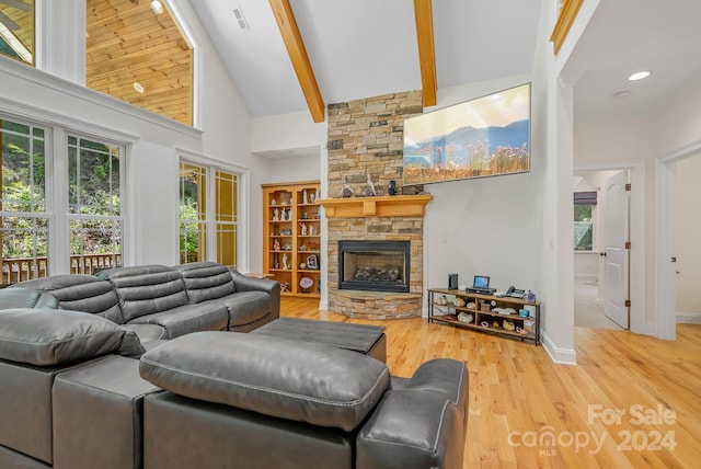 living room with high vaulted ceiling, a stone fireplace, light hardwood / wood-style floors, beamed ceiling, and built in shelves