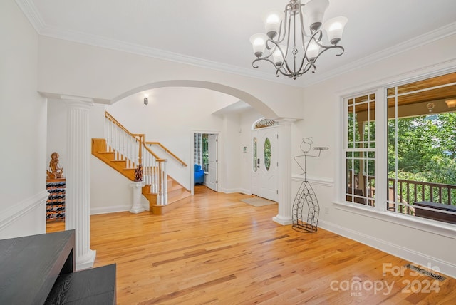 entryway featuring light wood-type flooring, ornate columns, crown molding, and a chandelier