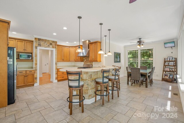 kitchen with light hardwood / wood-style flooring, ceiling fan, appliances with stainless steel finishes, crown molding, and wall chimney exhaust hood