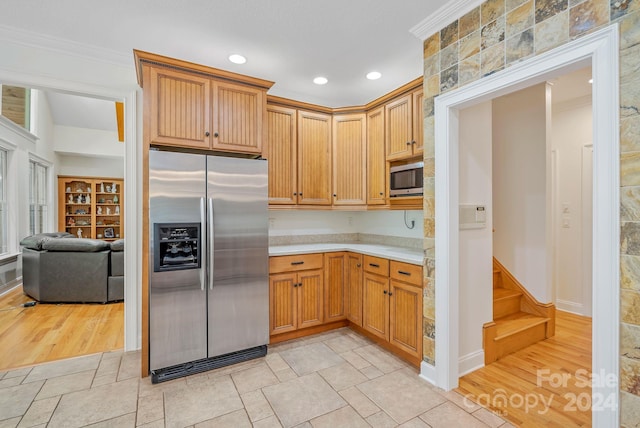 kitchen with appliances with stainless steel finishes, light wood-type flooring, light countertops, and ornamental molding